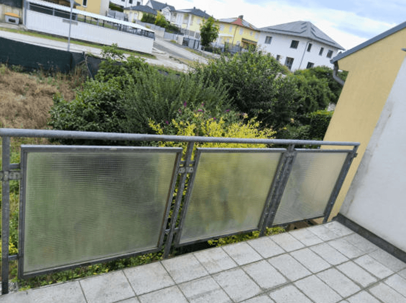 Balkon mit Fliesenboden und Blick auf die umliegende Wohngegend und viel Grün.