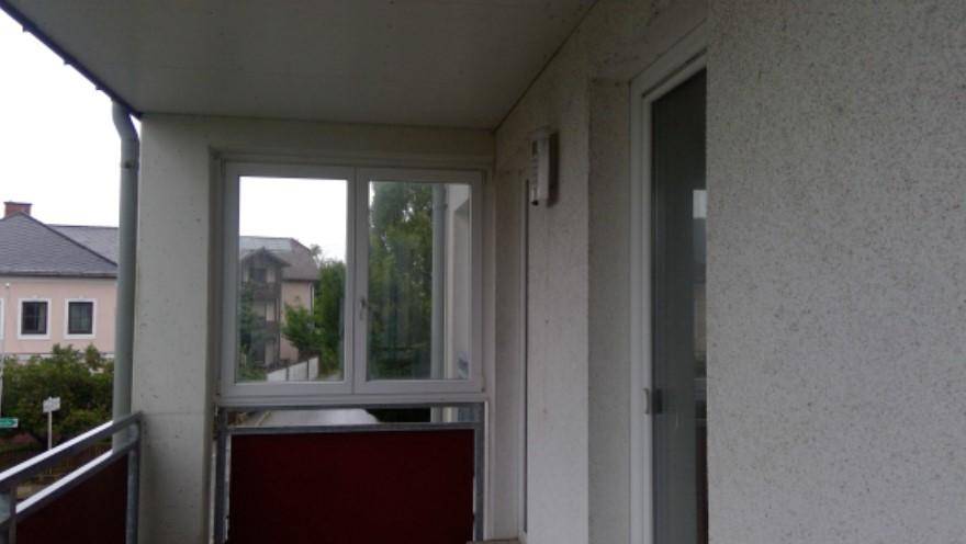 Kleiner Balkon mit Fenster und Blick auf die umliegenden Gebäude und Bäume.