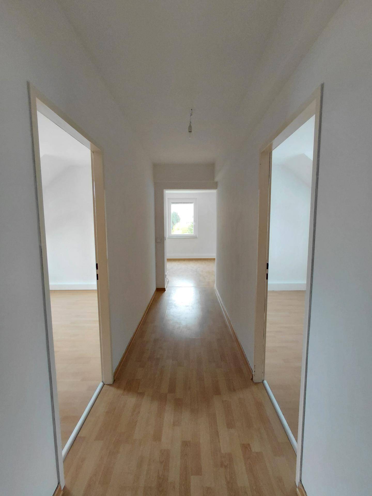 Langer, heller Flur mit Holzfußboden und offenen Türen zu weiteren Zimmern, mit Fenster am Ende.