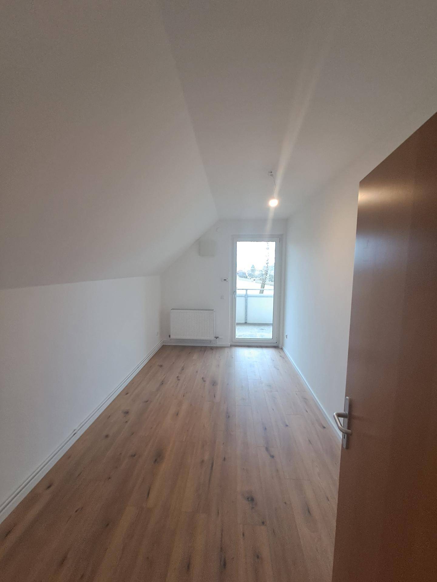 Dachgeschosszimmer mit Holzboden und Balkonzugang, bietet eine helle und gemütliche Atmosphäre.