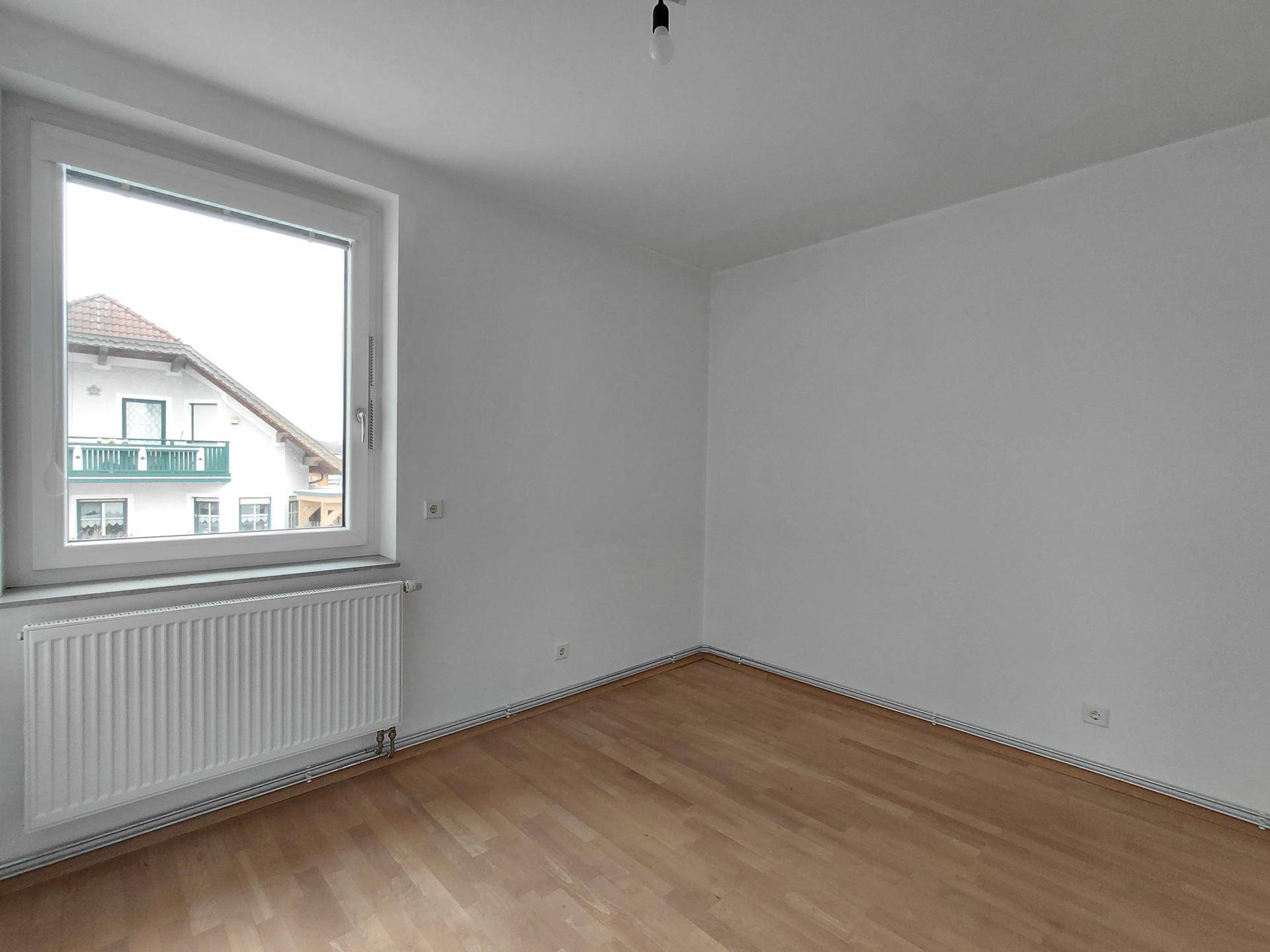 Leeres Schlafzimmer mit hellem Parkettboden, weiß gestrichenen Wänden und einem Fenster.