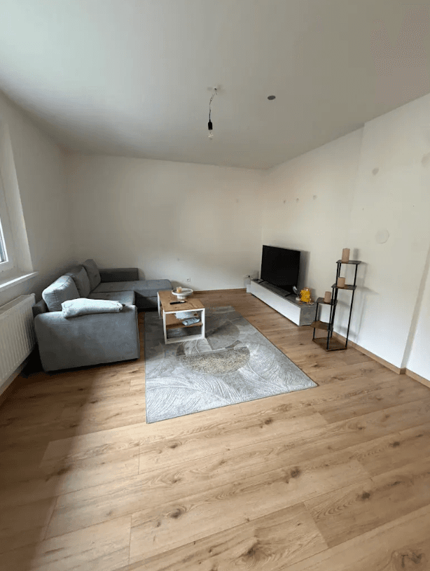 Geräumiges Wohnzimmer mit grauem Ecksofa, Teppich und hellem Laminatboden, modern dekoriert.