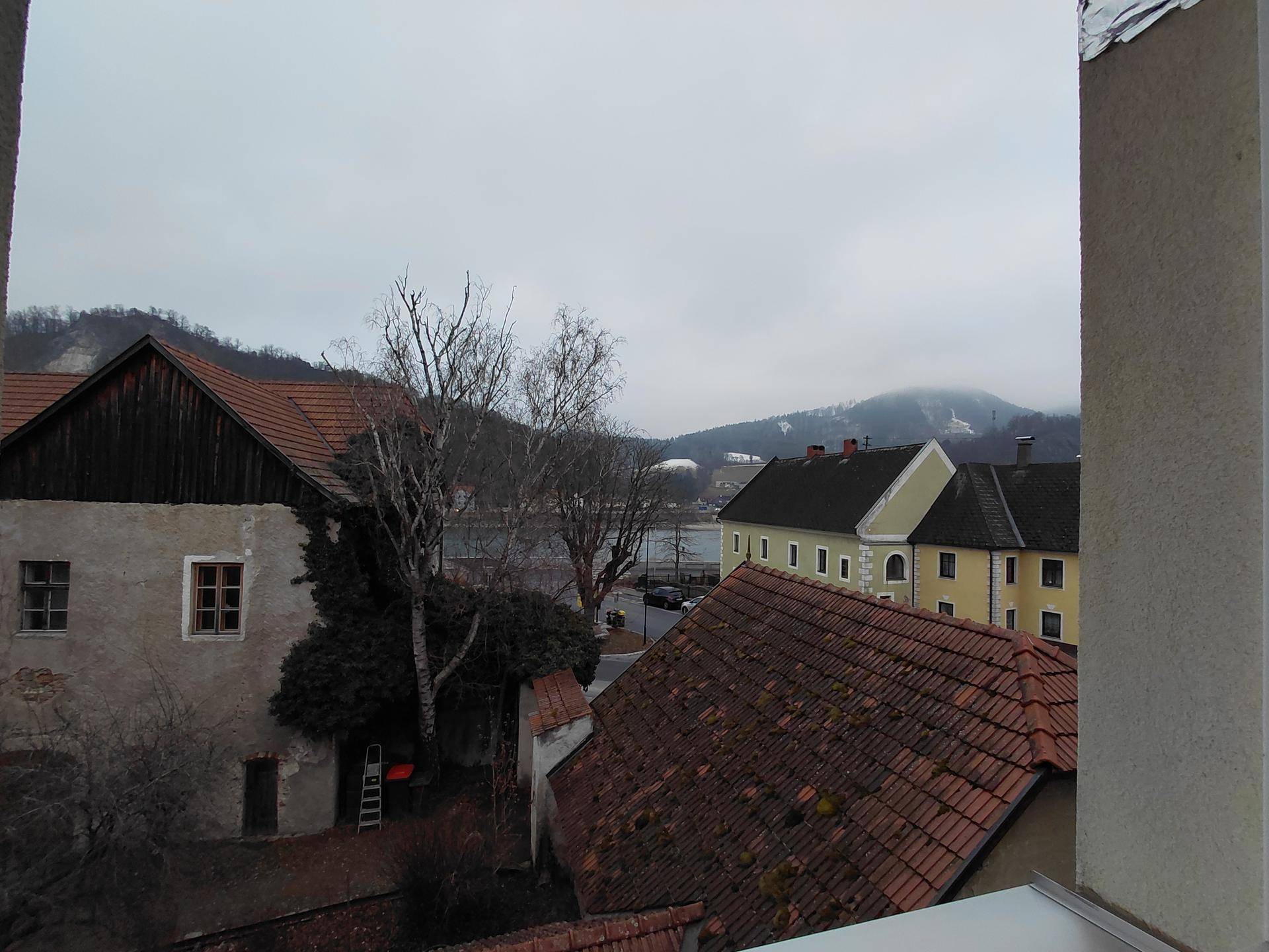 Blick aus dem Fenster auf die umliegende Bebauung, einen See und bewaldete Hügel in der Ferne.