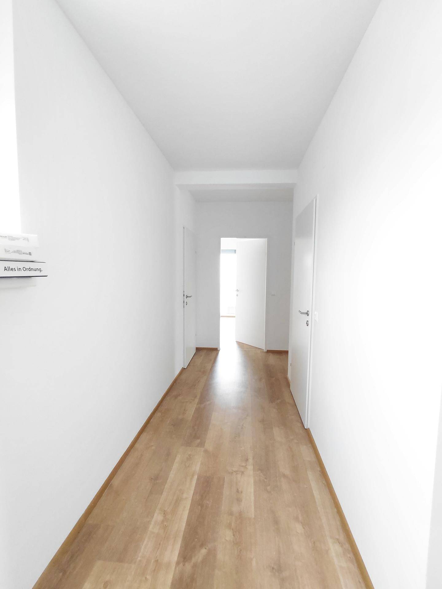 Langer, heller Flur mit Laminatboden und mehreren weißen Türen.