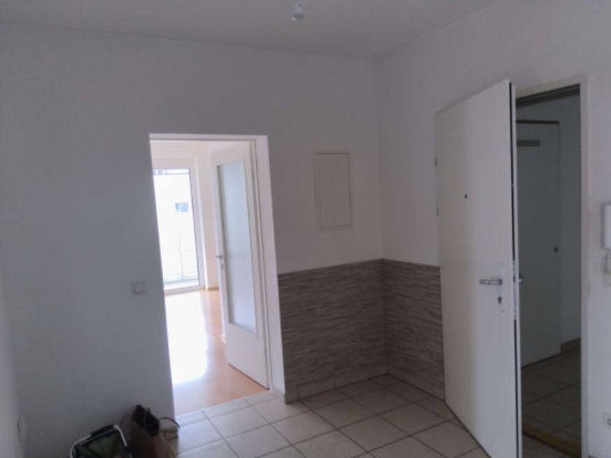 Eingangsbereich mit Fliesenboden und einer teilweise gefliesten Wand, die zu einem weiteren Raum führt.