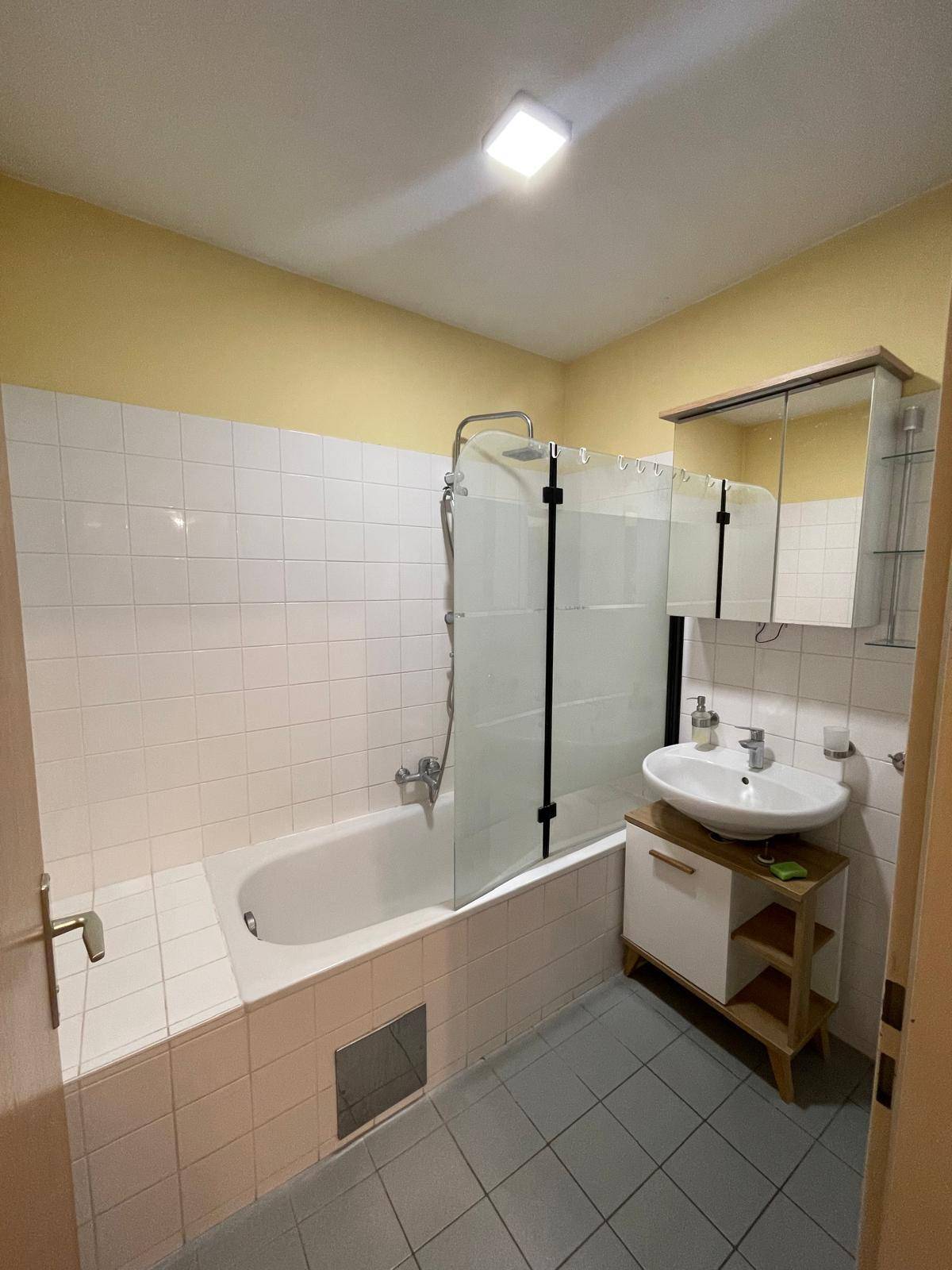 Badezimmer mit Badewanne, Duschabtrennung, Waschbecken und Spiegelschrank.