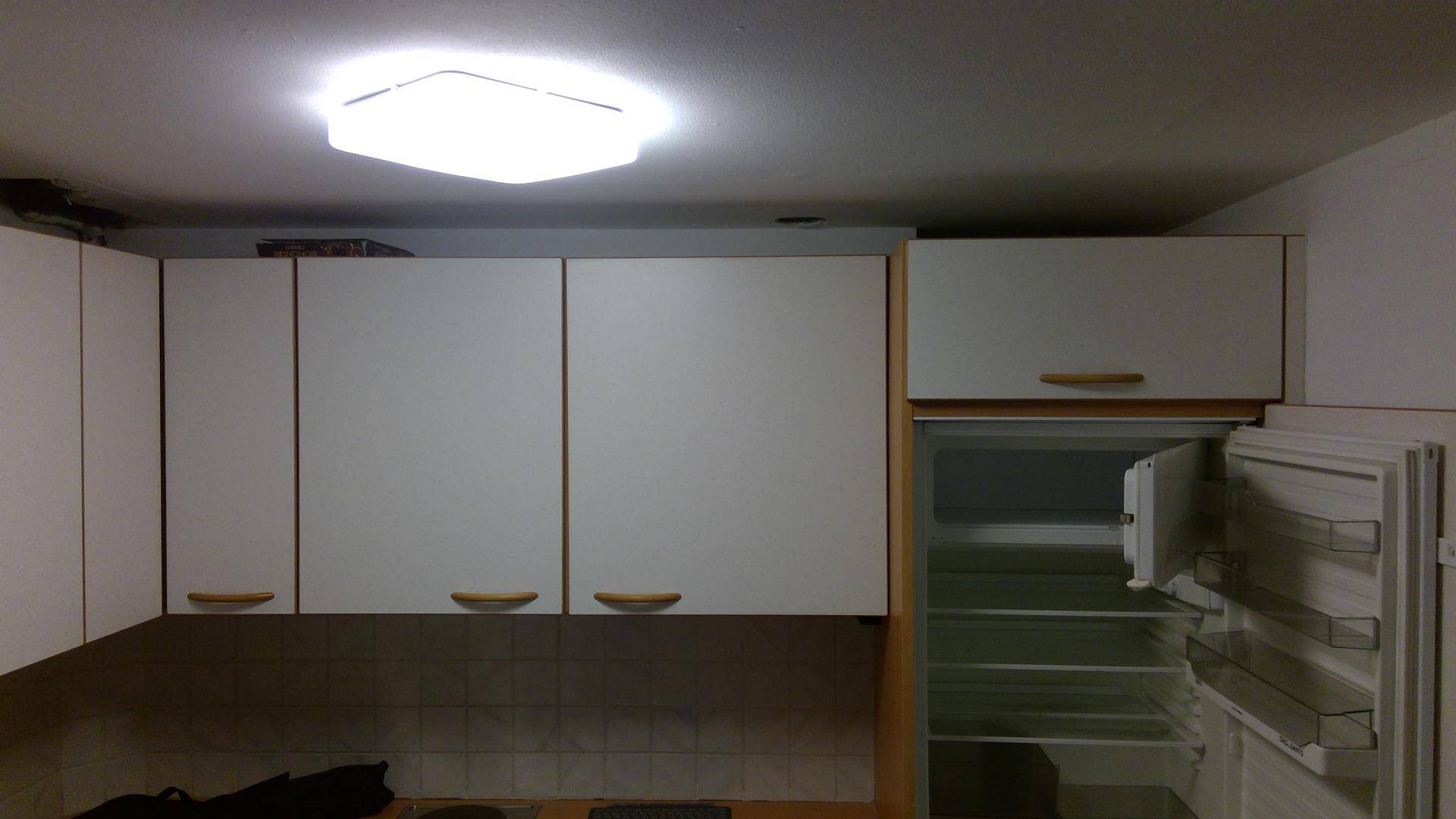 Obere Küchenschränke in Weiß mit Holzgriffen und integriertem Kühlschrank.