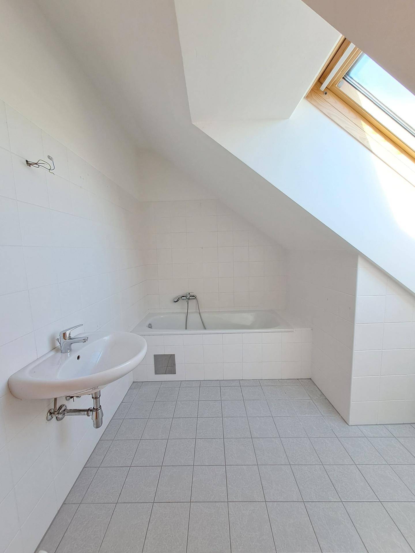 Helles Badezimmer im Dachgeschoss mit Badewanne, Waschbecken und Dachfenster.