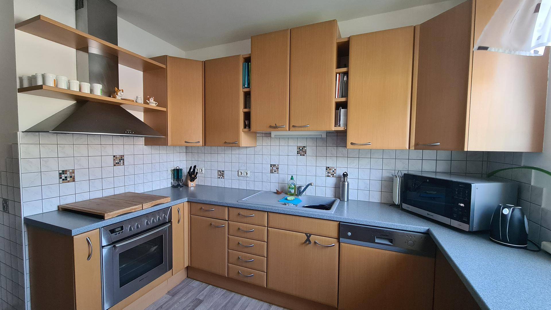 Funktionale Küche mit Holzschränken, grauen Arbeitsplatten und integrierten Geräten.