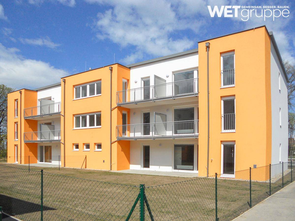 Modernes Mehrfamilienhaus mit leuchtend orangefarbener Fassade, weißen Akzenten und Balkonen unter blauem Himmel.