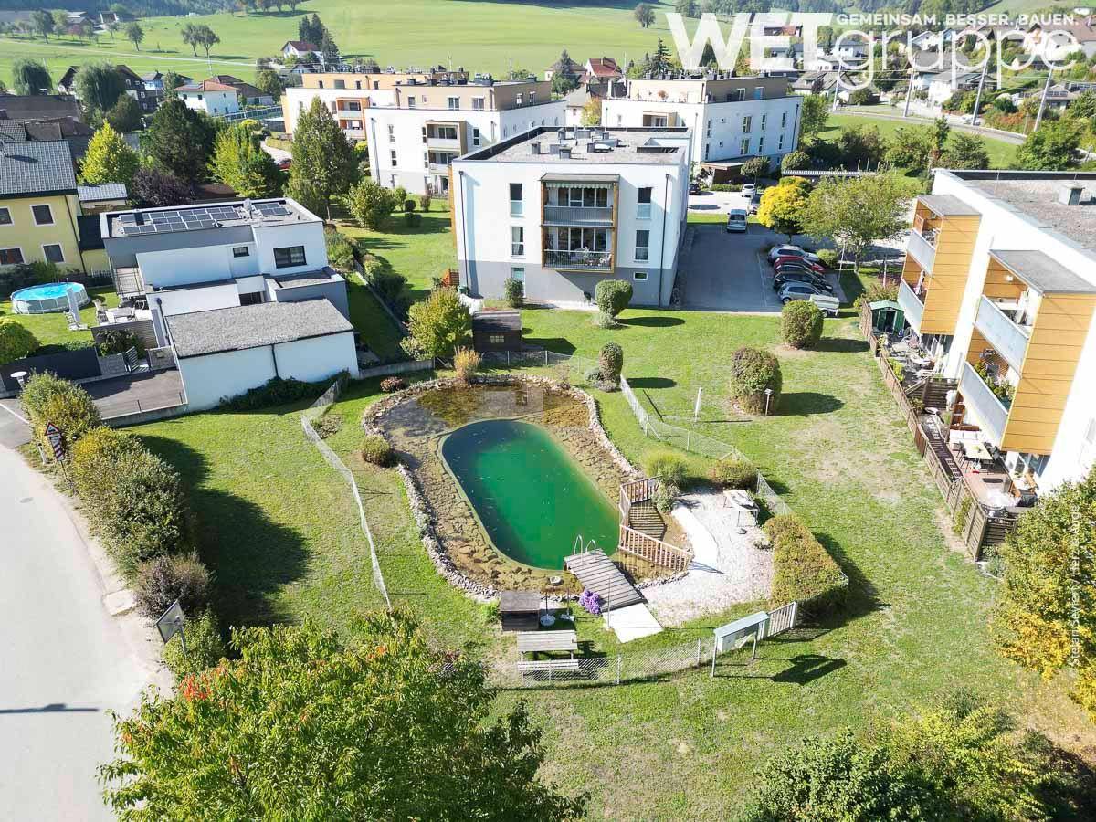 Weitläufige Ansicht der Wohnanlage mit Naturteich und umliegender Landschaft.