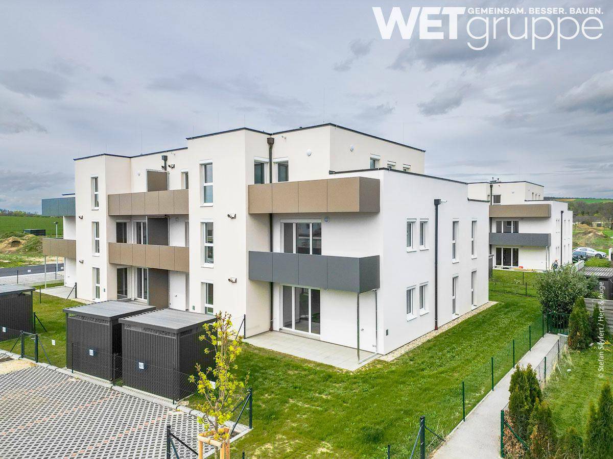 Neubau-Wohngebäude mit Balkonen und Terrassen, umgeben von Grünflächen und Parkplätzen.