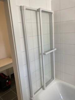Badezimmer mit Badewanne und Duschabtrennung, ausgestattet mit weißen Fliesen.