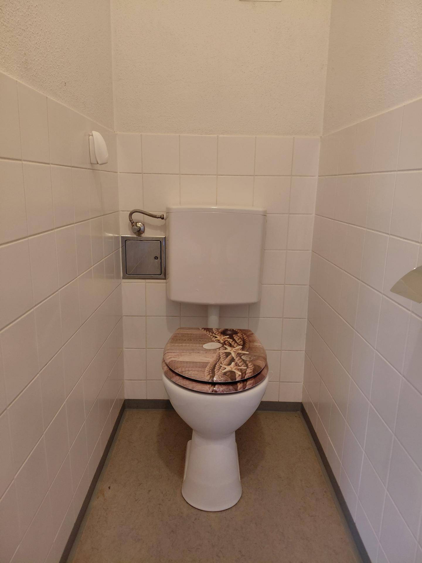 Kleines Gäste-WC mit weiß gefliesten Wänden und einer Toilette mit gemustertem Sitz.