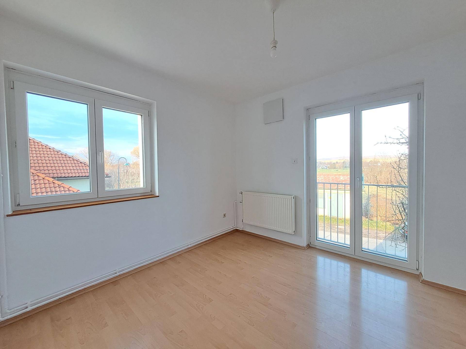 Helles Zimmer mit Parkettboden, weißen Wänden und Zugang zu einem französischen Balkon mit Aussicht.