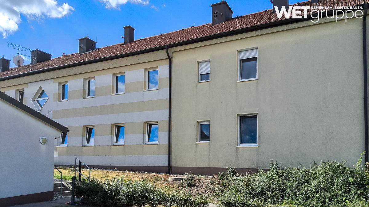 Seitenfassade eines Wohngebäudes mit mehreren Fenstern und einer kleinen Grünfläche davor.