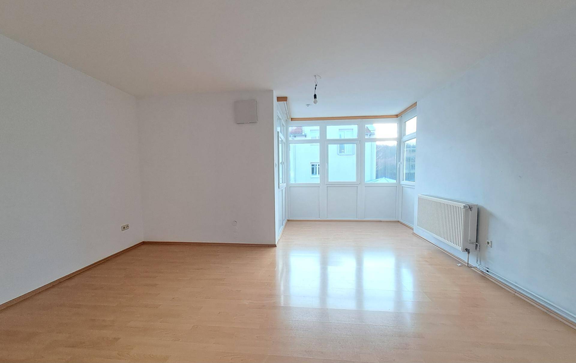 Geräumiges, leeres Zimmer mit hellem Parkettboden, weißen Wänden und einem sonnigen Erkerfensterbereich.