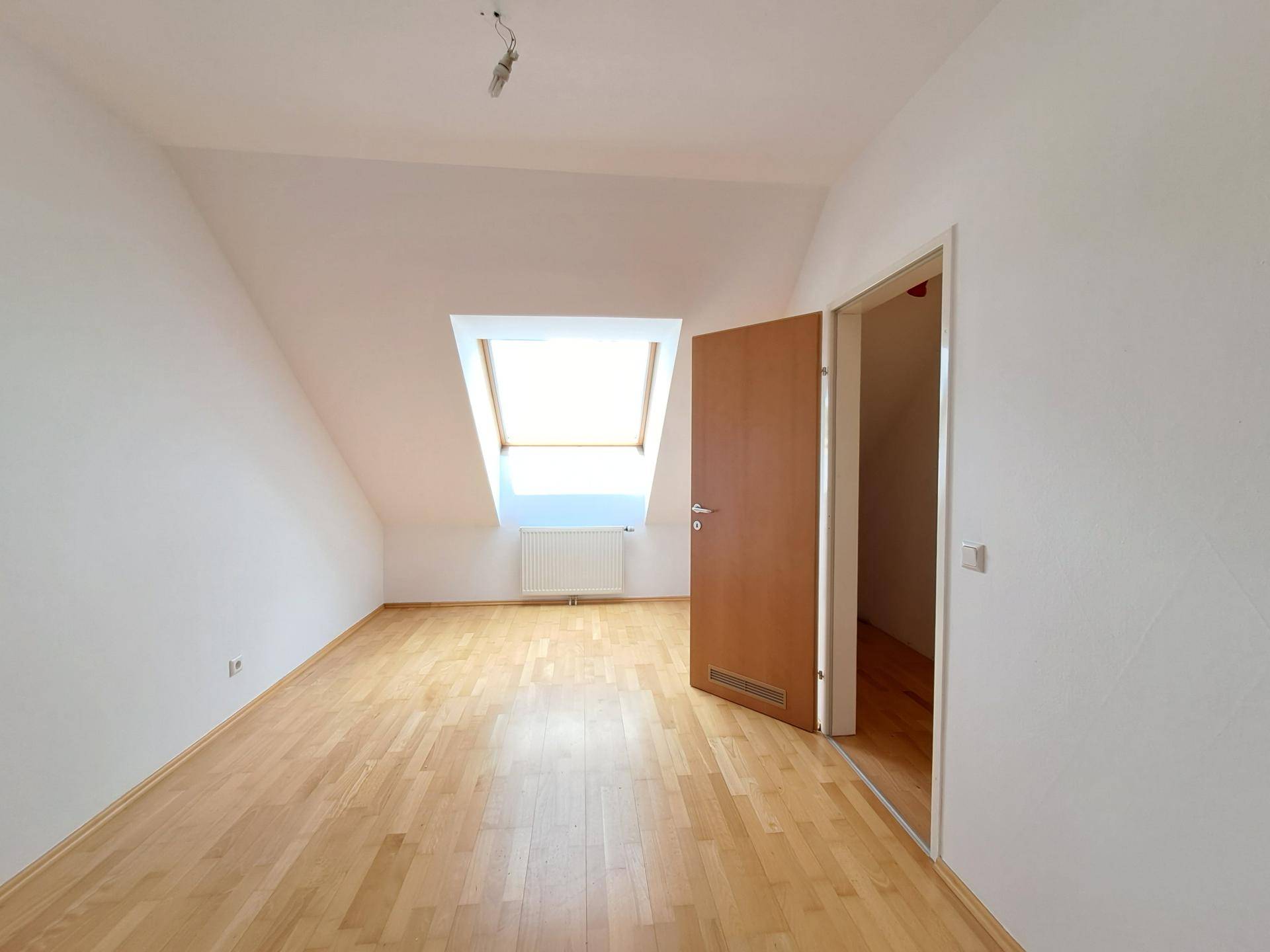 Helles Zimmer im Dachgeschoss mit Holzboden, Dachfenster und schrägen Wänden.