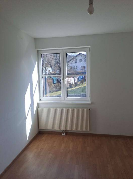 Helles Schlafzimmer mit Laminatboden und Blick auf die Nachbarschaft, gut belichtet durch ein Fenster.
