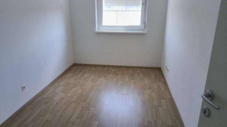 Leeres Schlafzimmer mit hellem Holzboden und einem Fenster, bereit zur individuellen Gestaltung.