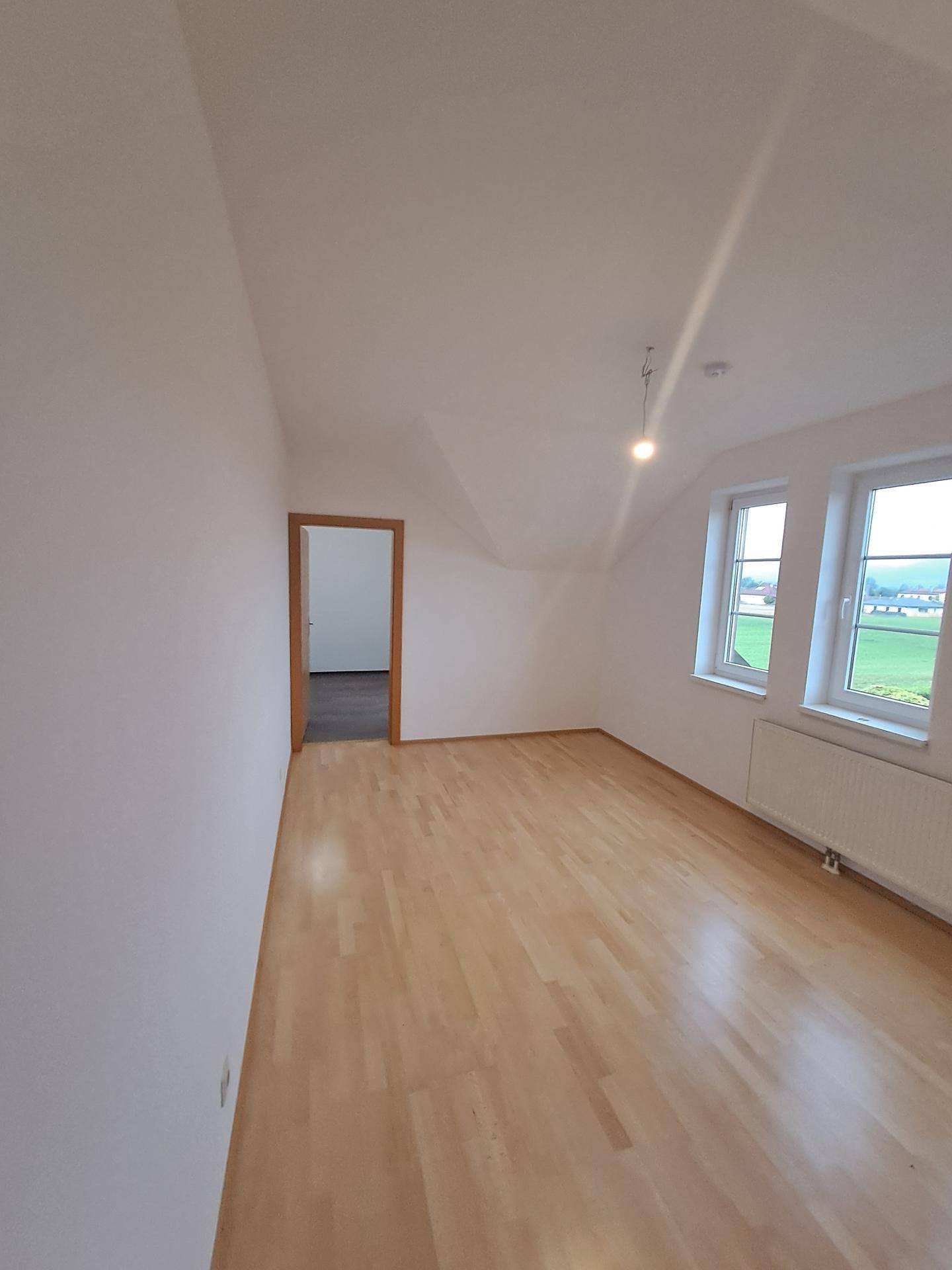 Geräumiges Dachgeschosszimmer mit hellem Laminatboden und Fenstern mit Blick auf die Landschaft.