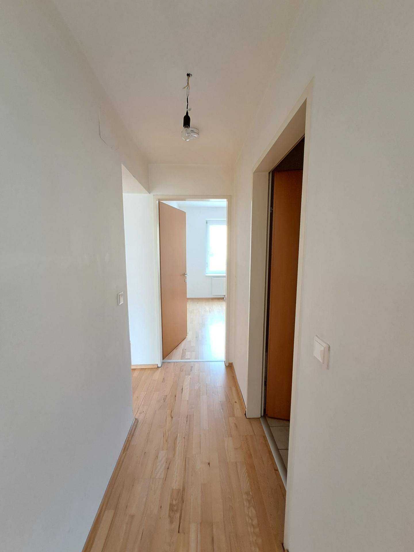 Langer, heller Flur mit Holzboden, der zu verschiedenen Zimmern der Wohnung führt.