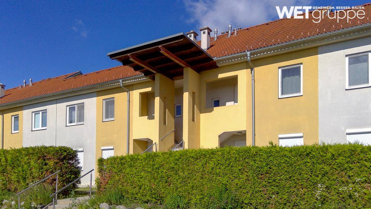Moderne Gebäudefassade mit gelben und grauen Farbakzenten und gepflegter Hecke.