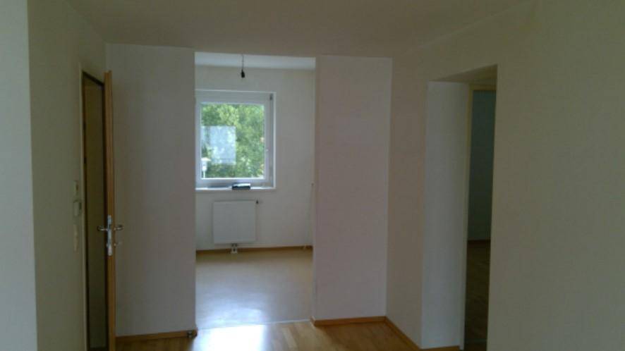 Heller Flur mit Holzboden, der zu einem weiteren Zimmer mit Fenster führt.