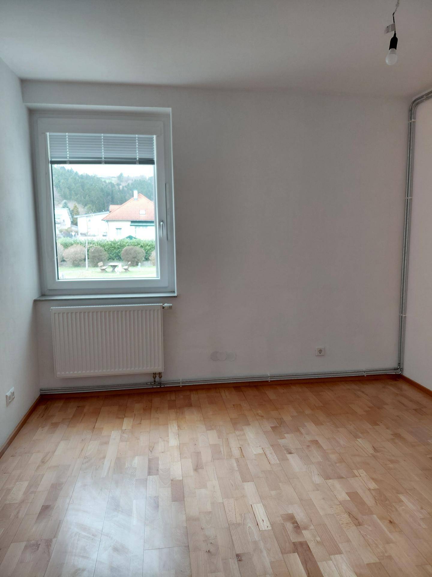 Helles Zimmer mit Parkettboden und Fenster, das einen Blick auf die Umgebung bietet.