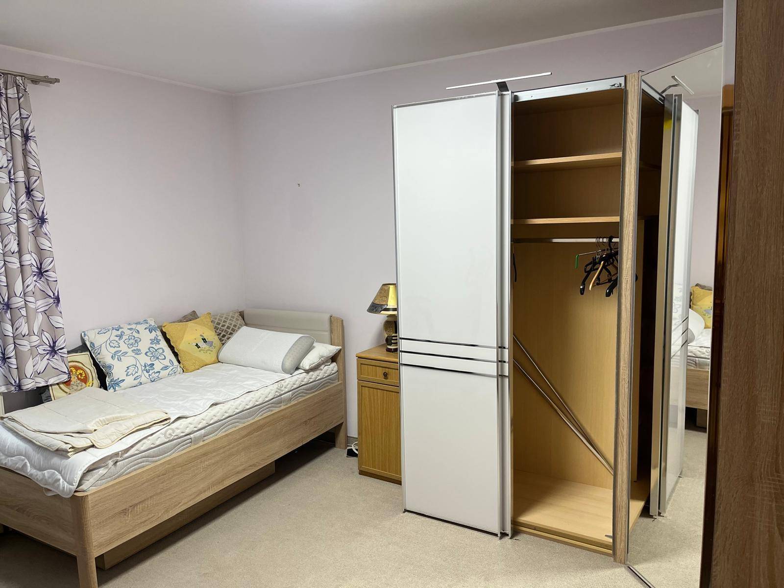 Schlafzimmer mit einem Einzelbett, Teppichboden und einem weißen Kleiderschrank mit Spiegeltüren.