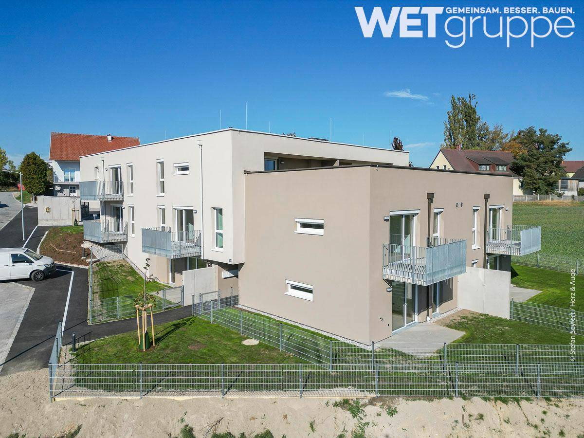 Ansicht des modernen Neubaus von der Seite mit Balkonen, Terrassen und angrenzender Grünfläche.