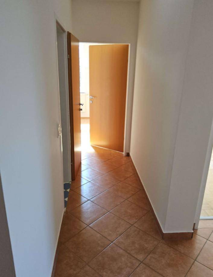 Heller Flur mit braunen Fliesen, weißen Wänden und Holztüren, die Licht hereinlassen.