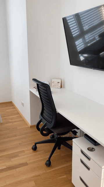 Funktionaler Arbeitsbereich mit Schreibtisch, Bürostuhl und Wandfernseher in hellem Raum.