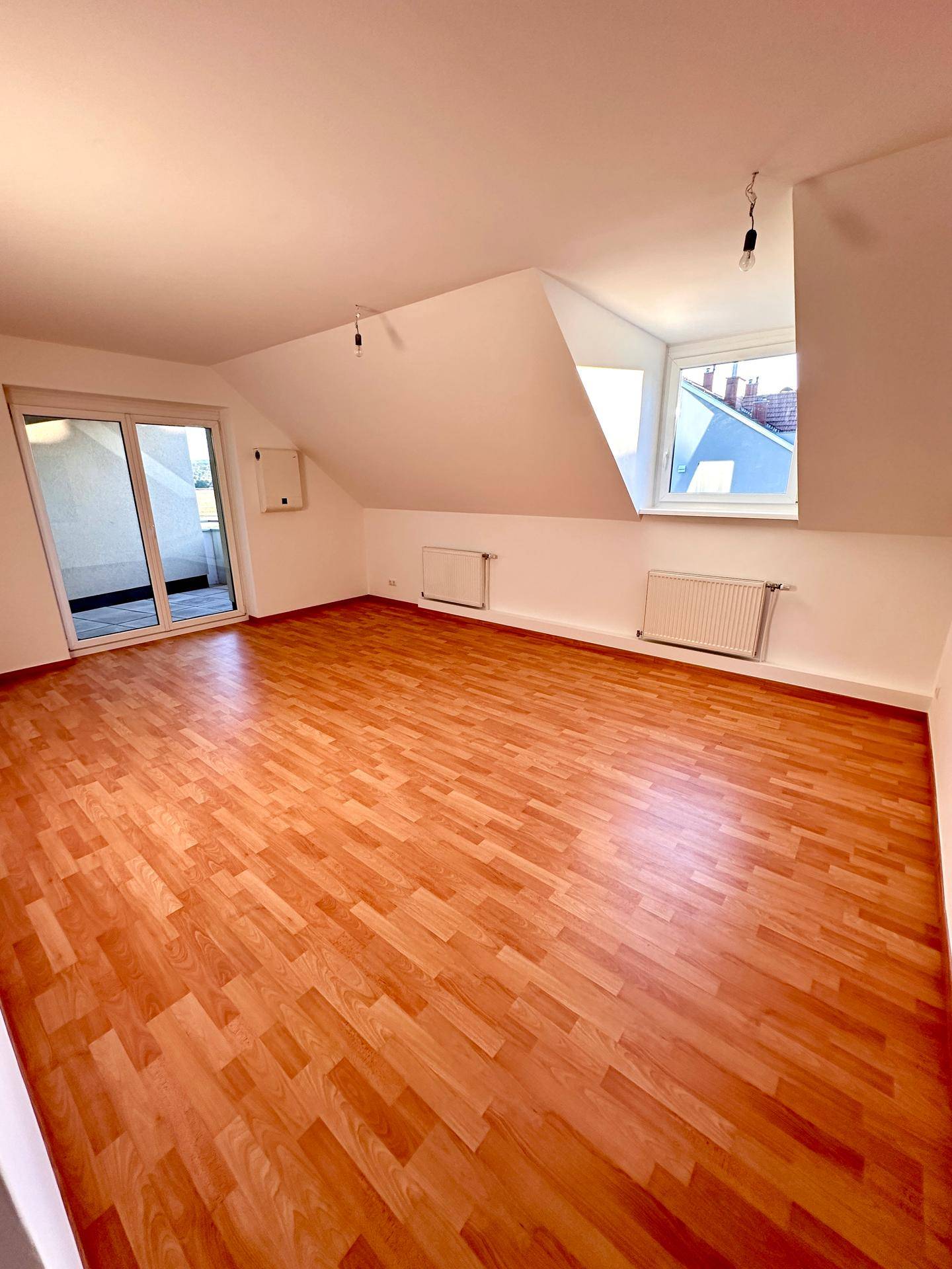 Heller Wohnraum mit Laminatboden, Dachschräge und direktem Zugang zum Balkon.