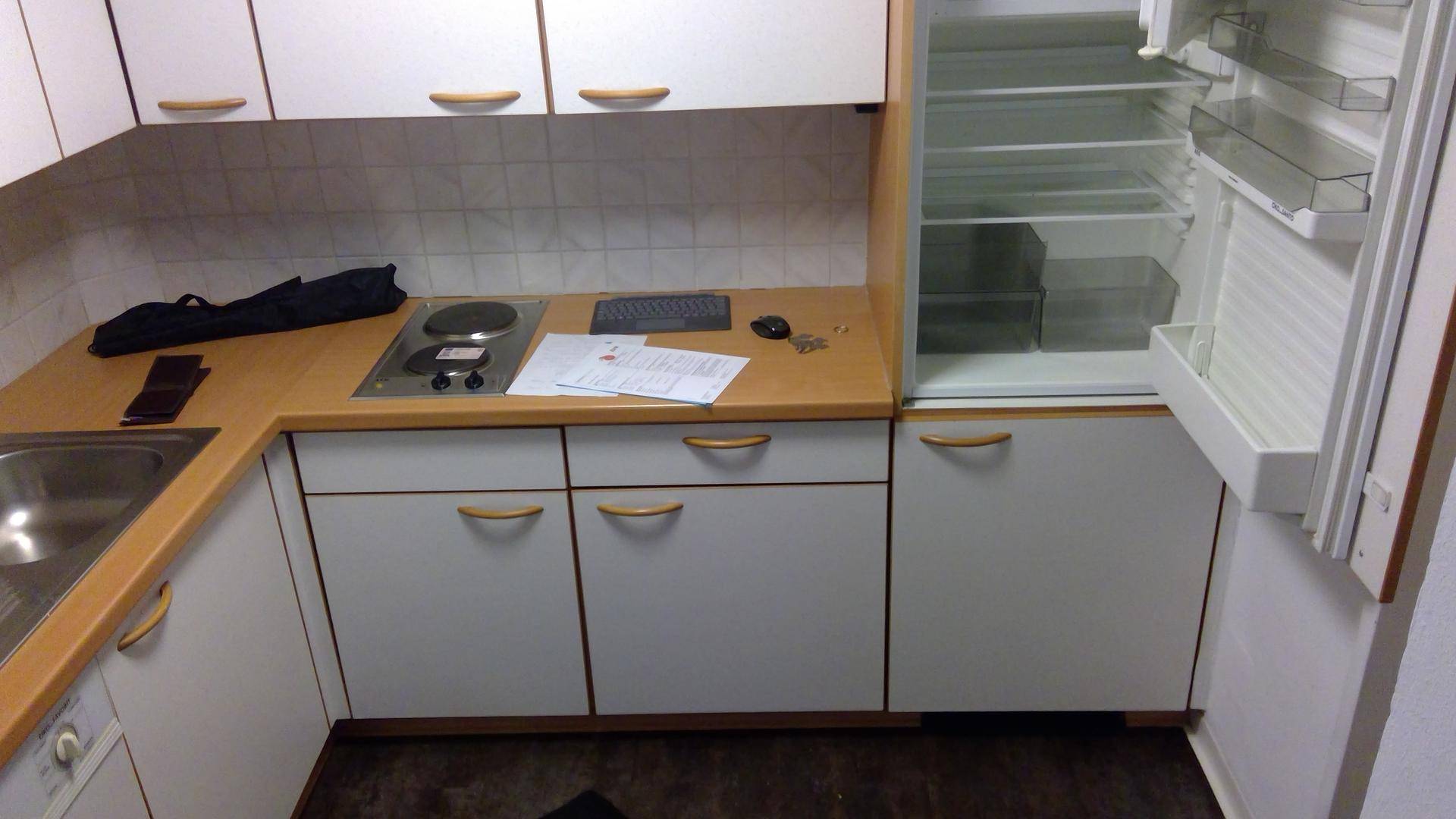 Kleine Einbauküche mit weißen Schränken, Holz-Arbeitsplatte und integriertem Kühlschrank und Herd.