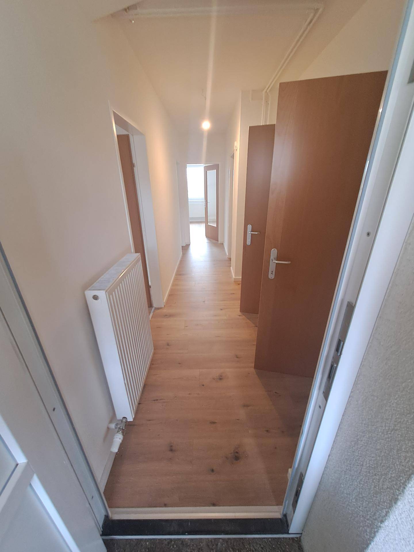 Heller Flur mit Holzboden und Zugang zu mehreren Zimmern, sorgt für eine offene Atmosphäre.