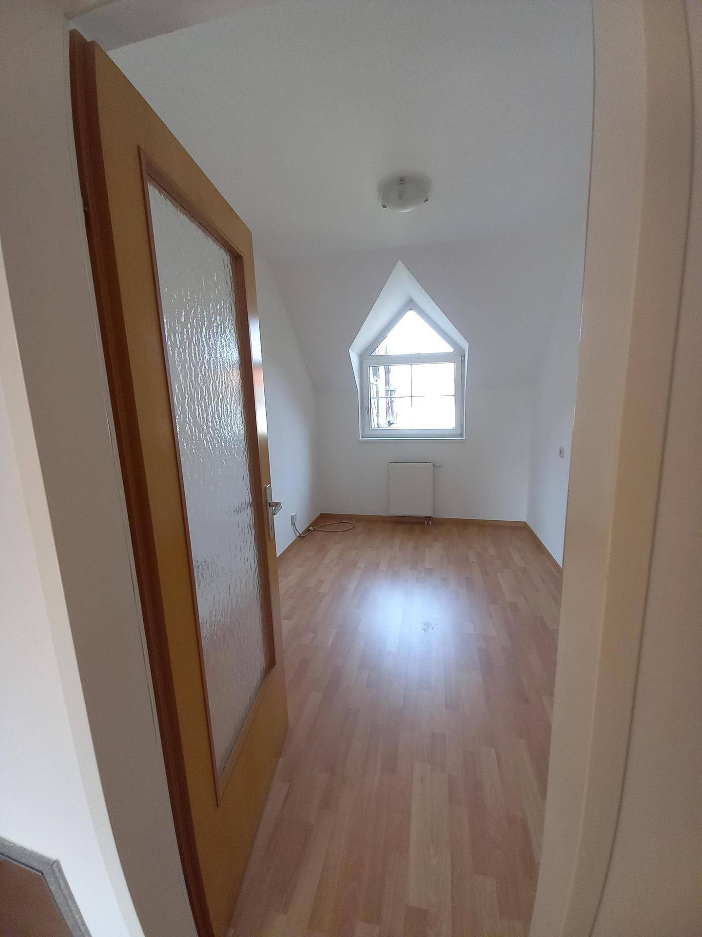 Helles Zimmer im Dachgeschoss mit Laminatboden und einem charakteristischen Giebelfenster.