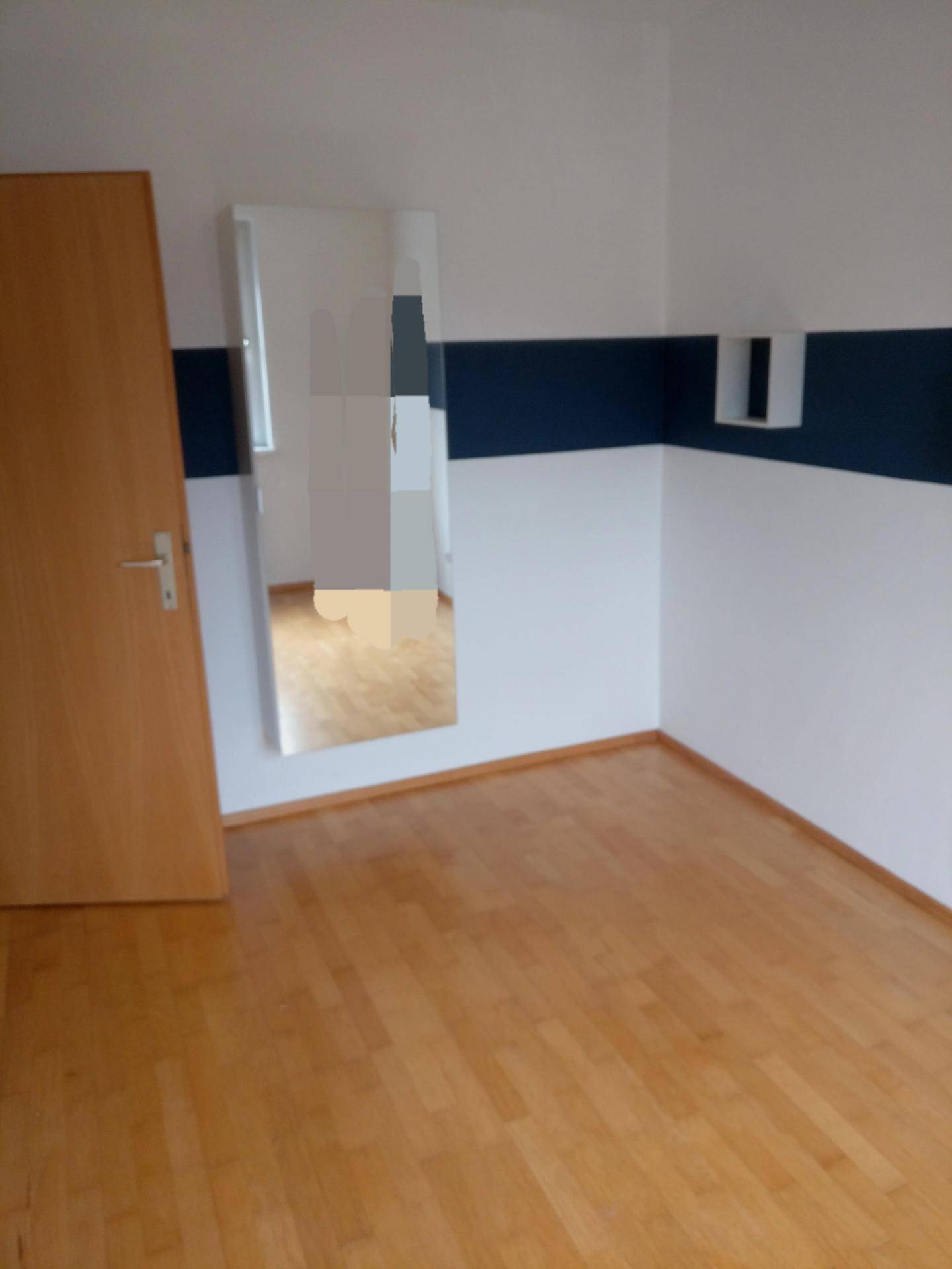 Leerer Raum mit Holzboden, weißen Wänden und einem blauen Streifen, mit einem Spiegel.