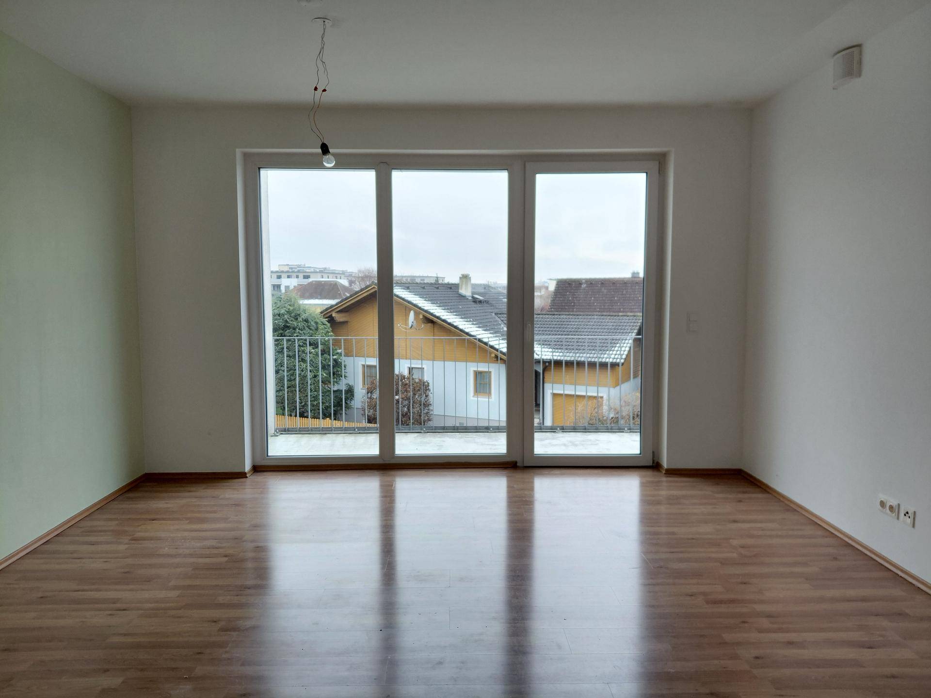 Heller Wohnraum mit Laminatboden und großem Fenster mit Balkonzugang, in gutem Zustand.