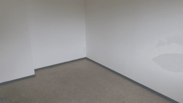 Ecke eines leeren Raumes mit hellem Bodenbelag und weißen Wänden, ohne weitere Details erkennbar.