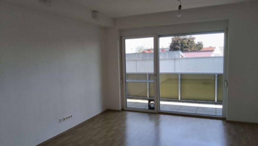 Helles Zimmer mit Holzboden und großem Schiebefenster, das zu einem Außenbereich führt.