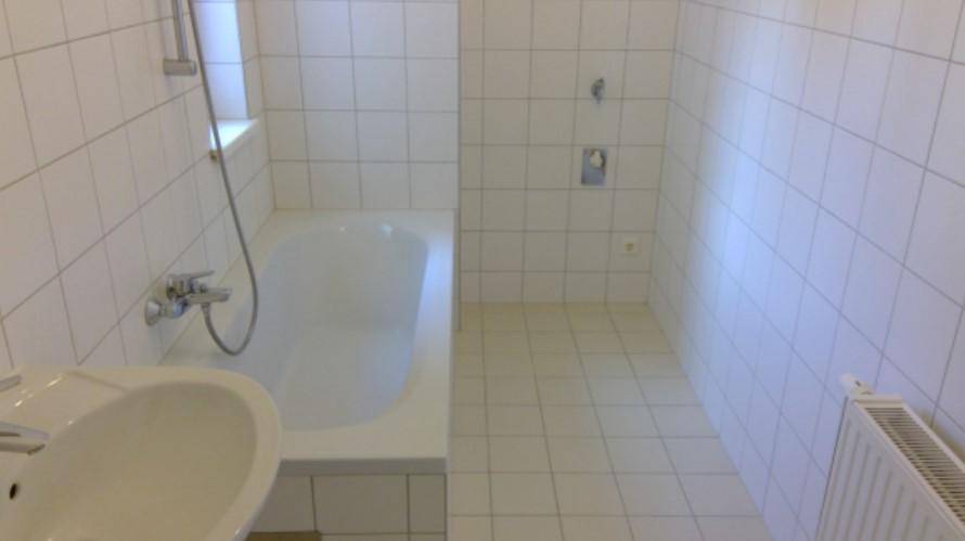 Badezimmer mit weißen Fliesen, Badewanne mit Duschfunktion und Waschbecken.
