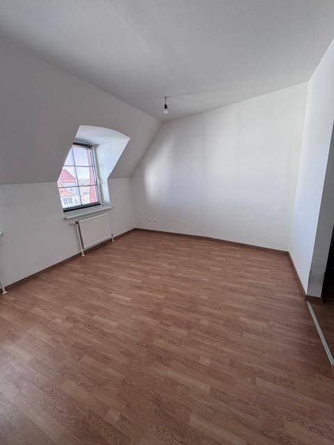 Geräumiges Zimmer mit Dachschräge, Laminatboden und Blick nach draußen.