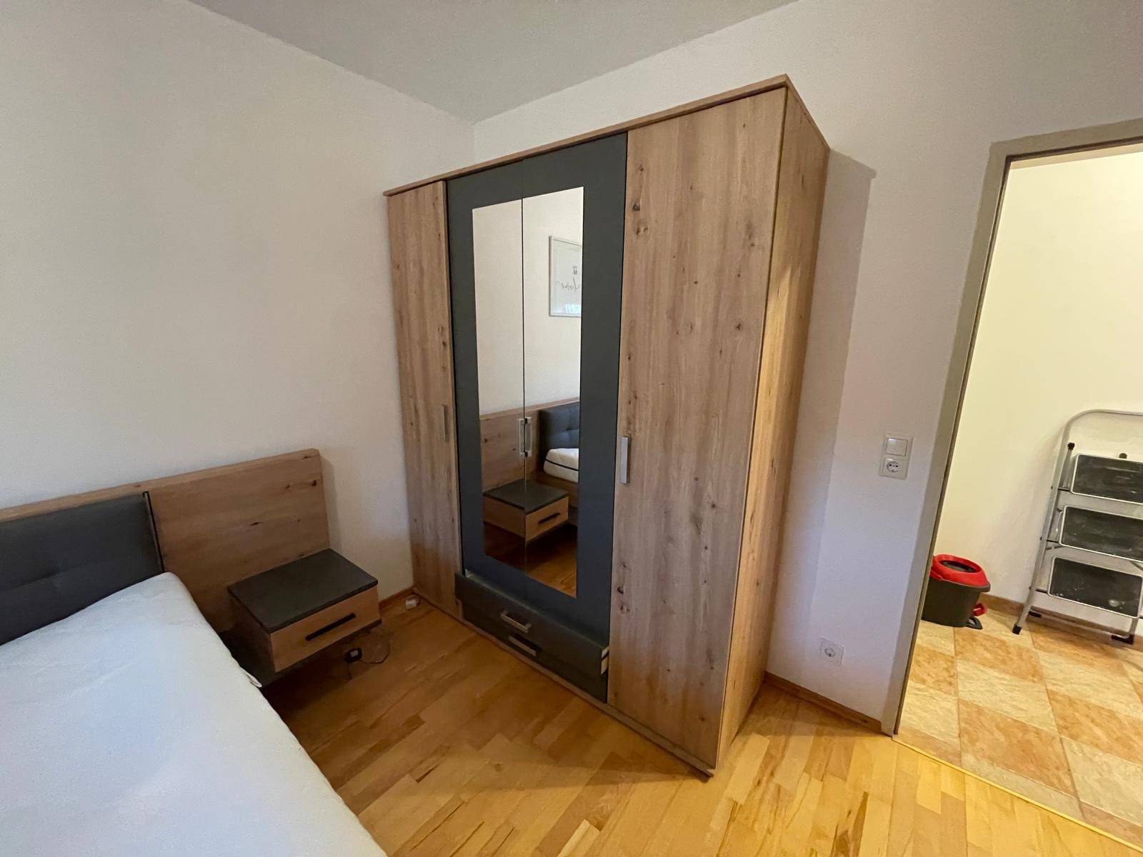 Schlafzimmer mit großem Kleiderschrank, Spiegeltür und Holzboden.
