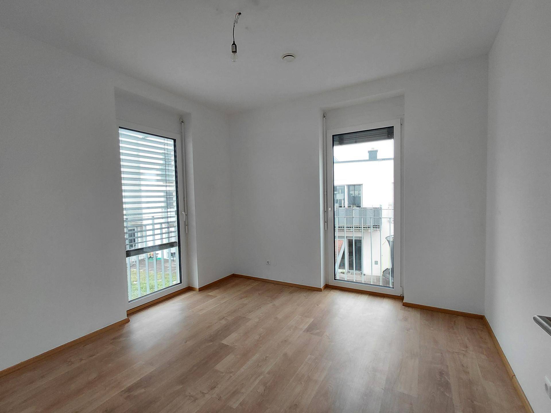Helles Zimmer mit Laminatboden, weißen Wänden und Zugang zu einem kleinen Balkon.