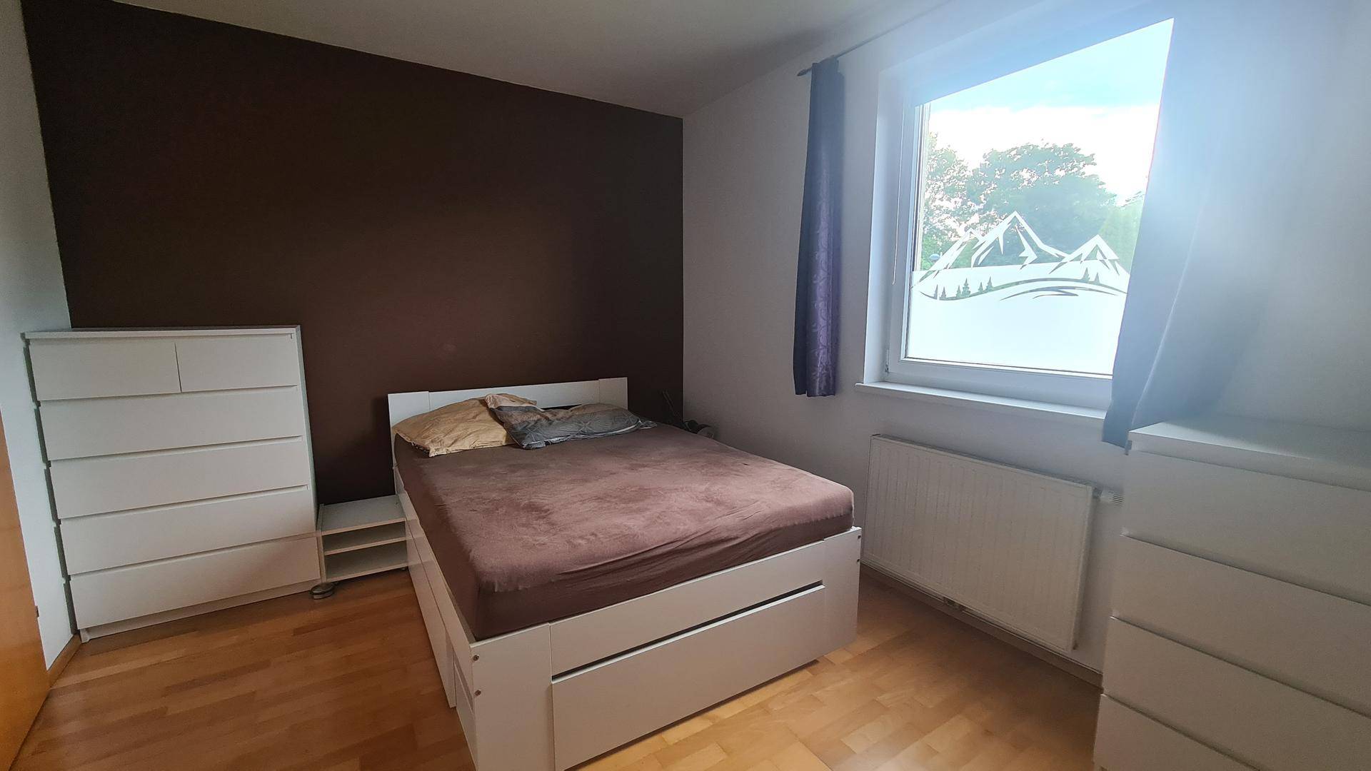 Helles Schlafzimmer mit Holzboden, weißem Bett, Kommoden und einer braunen Akzentwand.