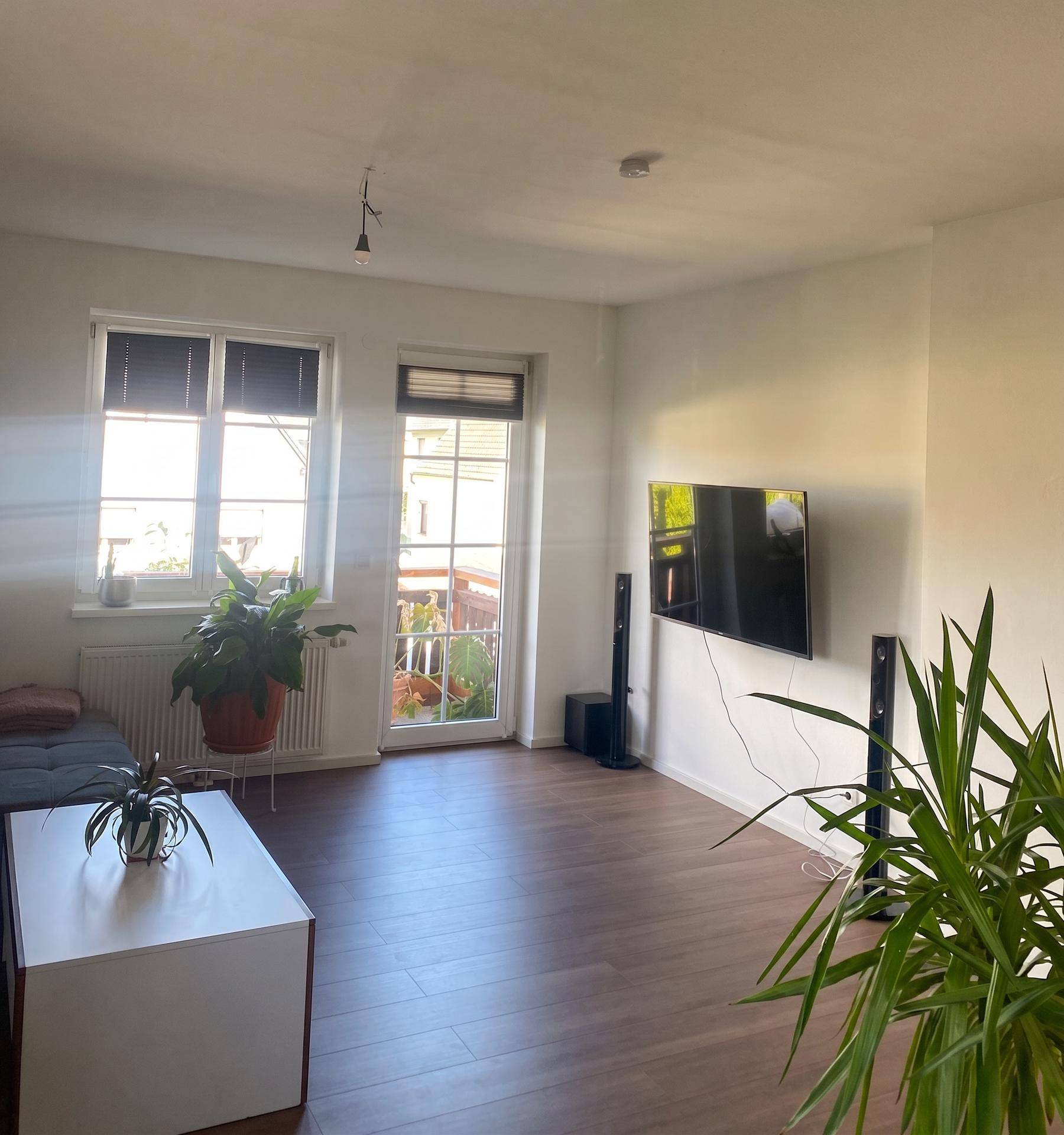 Gemütliches Wohnzimmer mit Fernseher, Sofa, Pflanzen und Zugang zu einem Außenbereich.