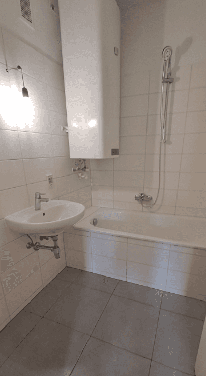 Funktionales Badezimmer mit weißen Fliesen, Badewanne, Waschbecken und einem Warmwasserboiler.