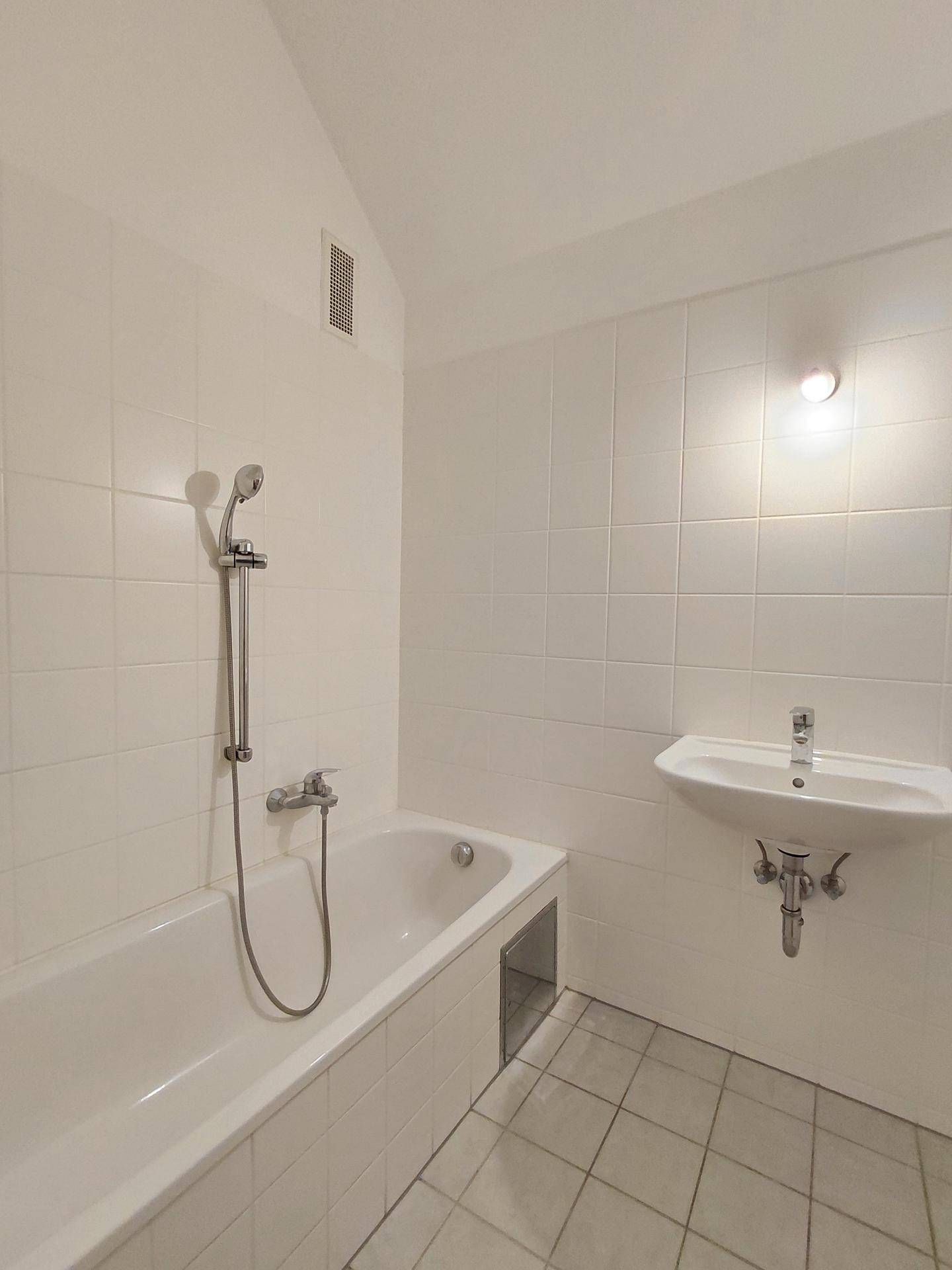 Helles Badezimmer mit weiß gefliesten Wänden, Badewanne mit Duschfunktion und Einzelwaschbecken.