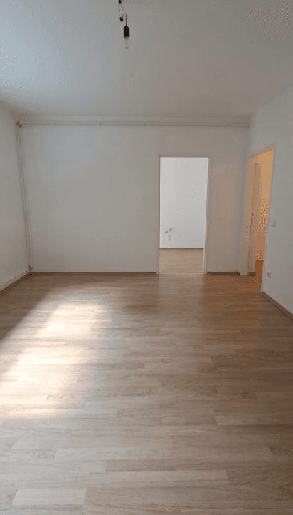 Geräumiges, unmöbliertes Zimmer mit Laminatboden und weißen Wänden, das vielseitig nutzbar ist.